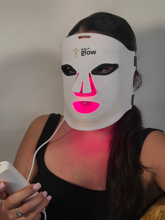 Beautiful woman with glowing skin wearing a LED face mask with visible branding against a plain background
